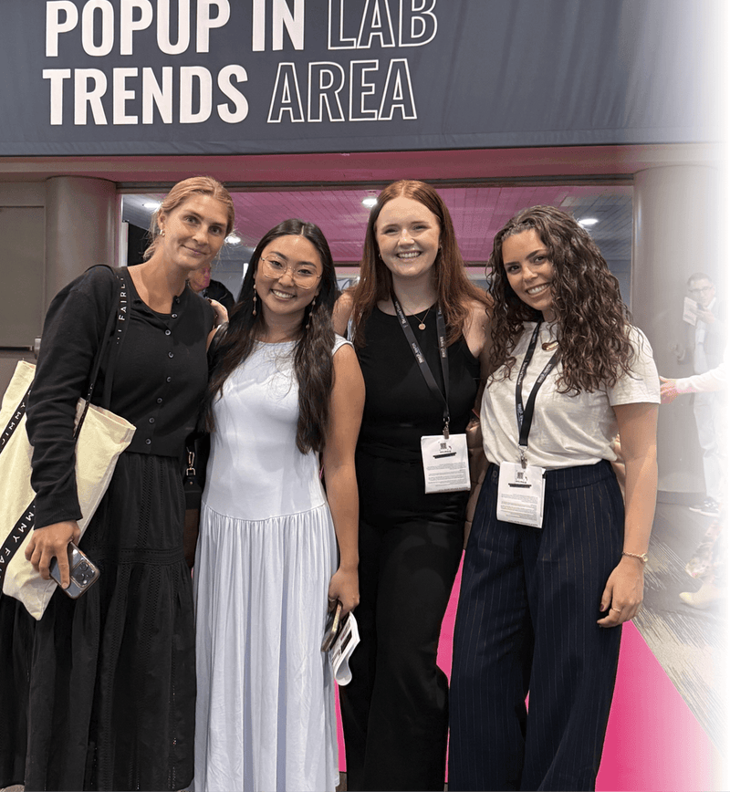 Four women posing together at what appears to be a conference or event booth, standing in front of a sign that reads 'POPUP IN LAB TRENDS AREA'.