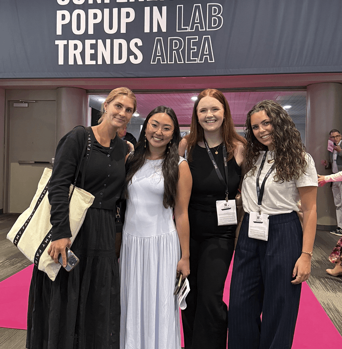 Four women posing together on a pink carpet in front of a convention center entrance with a sign that reads 'POPUP IN LAB TRENDS AREA'.